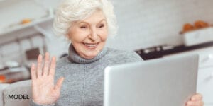 Smiling Mature Female Researching Questions About Dental Implants on Laptop